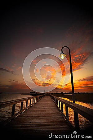 Wooden bridge over Shem Creek and a lamp under the orange-shaded sunset sky Stock Photo