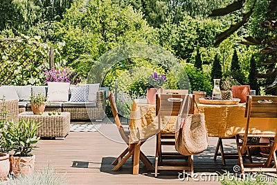 Wooden chairs at Dining table covered with orange tablecloth standing on wooden terrace in garden Stock Photo