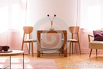 Wooden chairs at table with flowers in bright living room interior with armchair. Real photo Stock Photo