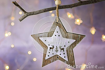 Wooden Christmas star ornament with reindeers hanging on dry tree branch. Shining garland golden lights. Beautiful background Stock Photo