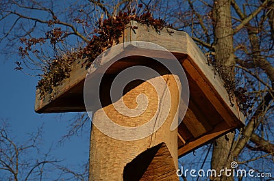 A wooden column made of roughly worked logs and the top has a green roof. green roof garden of micro dimensions above the birdhous Stock Photo