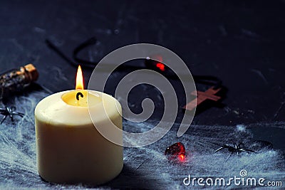 Halloween wooden cross lying next to a burning candle on a web with spiders and bats on a black background. horizontal Stock Photo