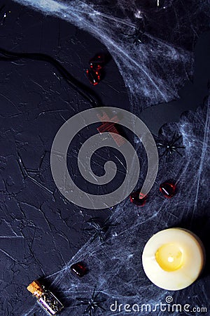 Halloween wooden cross lying next to a burning candle on a web with spiders and bats on a black background. vertical, flat lay, Stock Photo