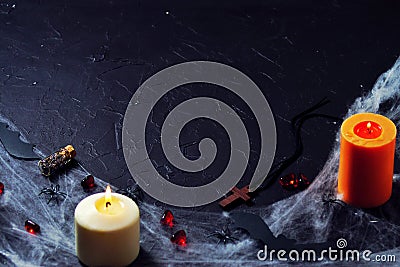 halloween wooden cross lying next to a burning candle on a web with spiders and bats on a black background. vertical Stock Photo
