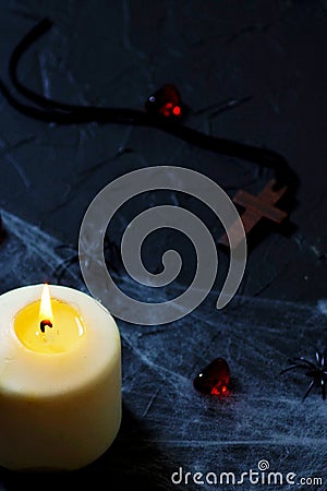 Halloween wooden cross lying next to a burning candle on a web with spiders and bats on a black background. vertical Stock Photo