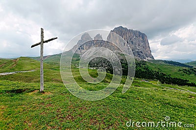 A wooden cross standing on the green grassy meadow at the foothills of rugged Langkofel-Plattkofel Mountains Stock Photo