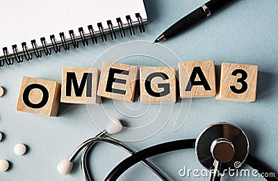 Wooden cubes with the inscription OMEGA 3 lie on the table. View from above. Nearby is a stethoscope, a notebook and scattered Stock Photo