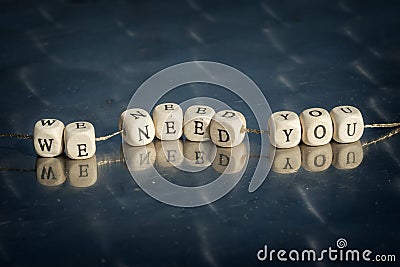Wooden cubes with we need you inscription strung on a thread on reflective table. Stock Photo