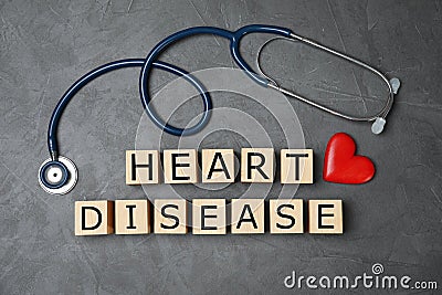 Wooden cubes with text Heart Disease and stethoscope on grey background Stock Photo