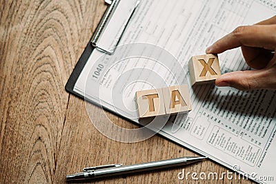 Wooden cubes with the word tax with US Income Tax Return forms 1040 to complete your tax legal. Editorial Stock Photo