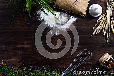 Wooden dark background on which lie a whisk, flour, a bag, a sieve, a jar, a jar of jam, straw, hay, oatmeal ears, sprinkled flour Stock Photo