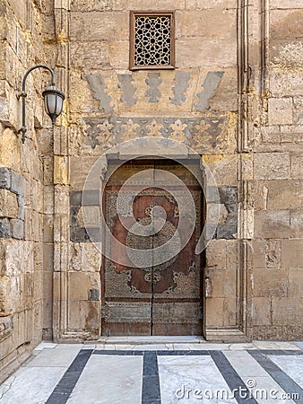 Wooden decorated copper plated door and stone bricks wall at the courtyard of Al-Sultan Barquq mosque, Old Cairo, Egypt Stock Photo