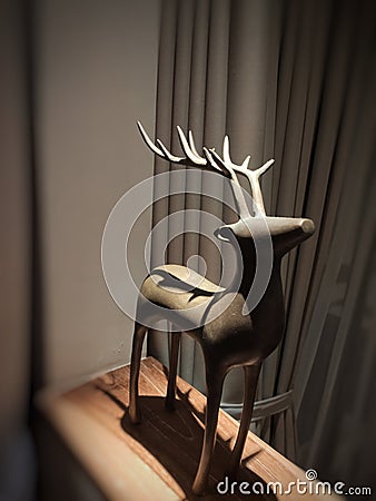 a wooden deer-shaped statue that stands upright under a bedroom lamp Stock Photo