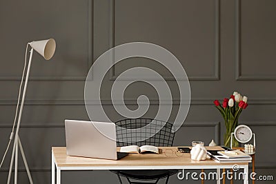 A wooden desk with a notebook and a pen, glasses, a laptop, a glass of water, next to which there is a white lamp, and behind Stock Photo
