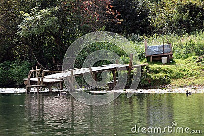 Wooden dilapidated improvised homemade river pier made of wooden boards and support poles at local river bank edge Stock Photo