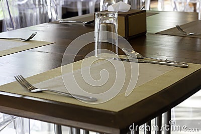 Wooden dining table and plastic chairs and industrial lamp at hotel and light from window, empty table with glasses, fork and Stock Photo