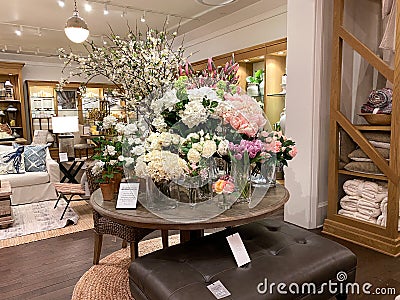 A wooden dining table and wicker chair with floral display at a Pottery Barn at an indoor mall in Orlando, Florida Editorial Stock Photo