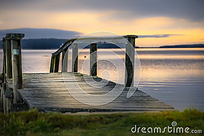 Wooden dock extends out into the tranquil lake at sunset Stock Photo