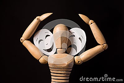 Wooden doll on hinges holds a mask in hands and covers her face on a black background Stock Photo