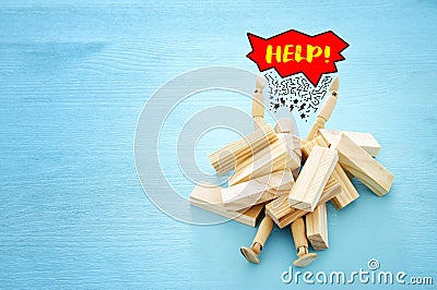 wooden dummy buried under stack of domino blocks asking for help. concept of stress, trouble and deadline overwork. Stock Photo