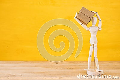 wooden dummy figure holding present box over yellow background. Stock Photo