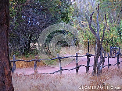 Wooden fence with red sand dirt road and dry grass at Okonjima Nature Reserve, Namibia Stock Photo