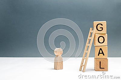 The wooden figure of a man stands near a tower of cubes with the word goal. The concept of achieving the goal, dedication Stock Photo