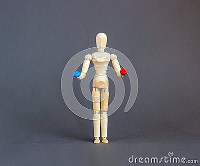 Wooden figure of a mannequin holding a red pill and blue pill on a grey background. Coronavirus, pandemic and epidemic concept. Stock Photo