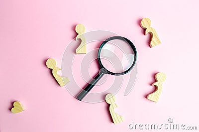 Wooden figures of lonely people around a magnifying glass. Search for love and creation of strong love relationships. Stock Photo