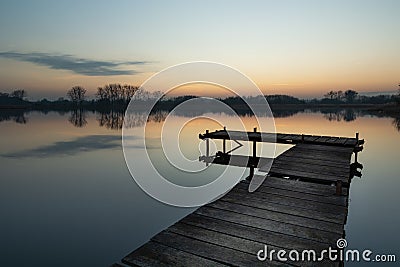 Wooden fishing platform on a calm lake and reflection of clouds in the water Stock Photo