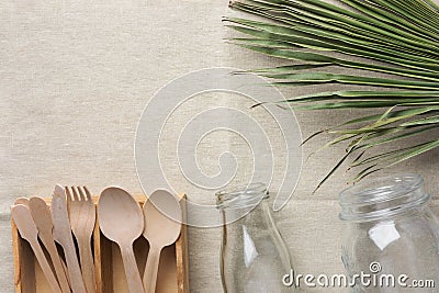 Wooden flatware cutlery crystal jar bottle green palm leaf on linen fabric background. Plastic-free alternatives zero waste Stock Photo