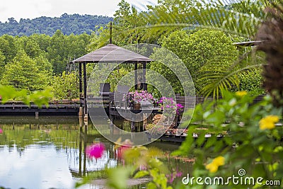 Wooden gazebo with sun loungers for relaxing on a terrace with flowers next to a lake on the tropical island of Thailand Stock Photo