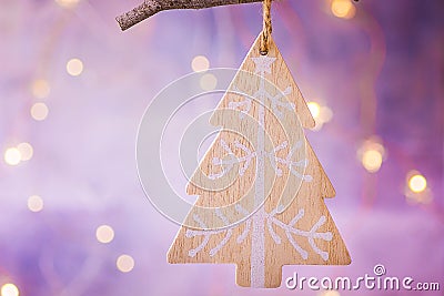 Wooden handmade Christmas tree ornament hanging on branch. Shining garland golden lights. Purple background. Magical atmosphere. Stock Photo