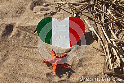 Wooden handmade heart in the colors of flag of Italy green, white and red with red starfish in golden sand on beach Stock Photo