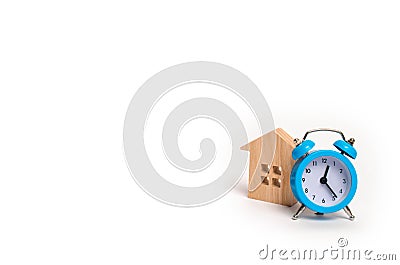 Wooden house and blue alarm clock on a white background. The concept of rent housing monthly and hourly. Temporary affordable acco Stock Photo