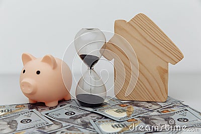 Wooden house, piggy bank and clock on dollar banknotes. Investment, savings and real estate Stock Photo