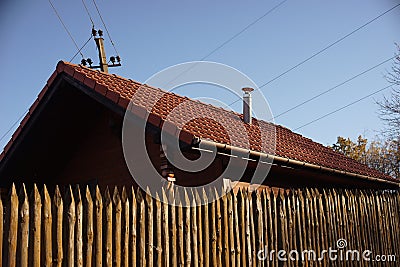Wooden house with red tiled roof and blue sky. Fence made of sharp wooden stakes Stock Photo