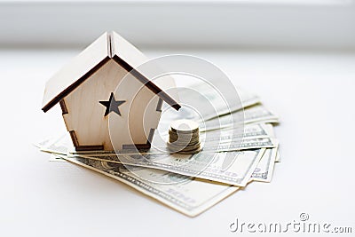 Wooden house stands on a pile of paper bills dollars as a symbol of mortgage on white background. Saving money Stock Photo