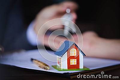 Wooden house on the table background with Real-estate agent giving keys to new property owners after signing contract for realty Stock Photo