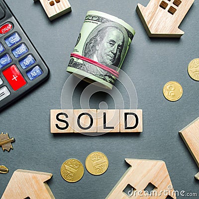 Wooden houses, a calculator, keys, coins and blocks with the word Sold. Concept of selling a house, apartment. Stock Photo