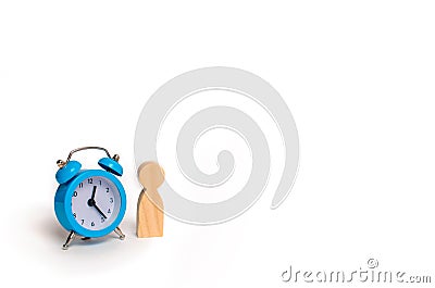 Wooden human figure stands near a blue alarm clock on a white ba Stock Photo