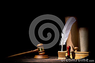 Wooden judge gavel hammer, old inkstand with feather quill, blotter, seal near scrolls against black background. Dramatic light. Stock Photo
