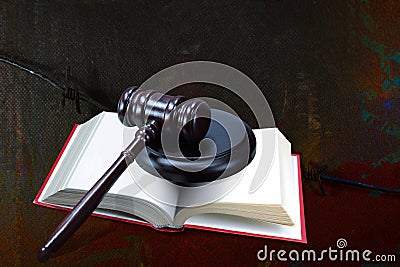 Wooden judge gavel and red book on barbed wire background as symbol of of rule of law with judge`s gavel, justice with judge`s ga Stock Photo