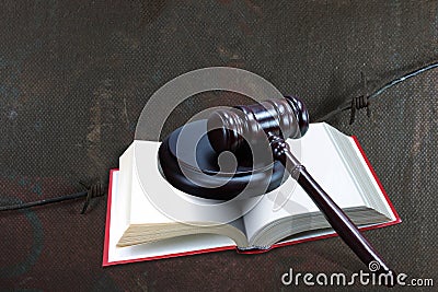 Wooden judge gavel and red book on barbed wire background as symbol of of rule of law with judge`s gavel, justice with judge`s ga Stock Photo