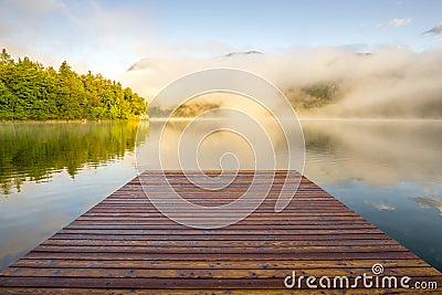 Wooden landing jetty at sunrise. Foggy morning at lake Bohinjsko, Slovenia. Stock Photo