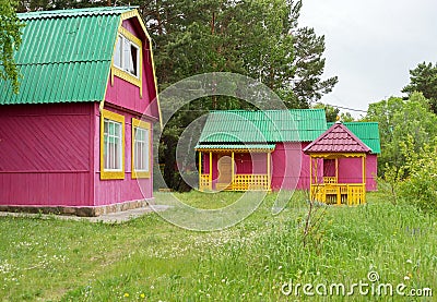 Wooden little cottages for tourists stand in the parkland in a blooming meadow among the trees on a summer day Stock Photo