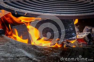 A wooden log burns brightly in a wood-fired grill. Circle wood-fired grill with steel grate for outdoor cooking Stock Photo