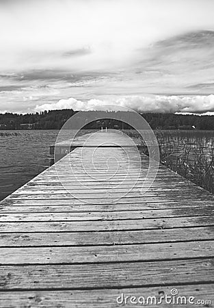 Wooden long empty pier on the lake shore in black and white. Stock Photo