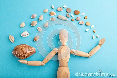Wooden mannequin juggling sea shells on blue pastel background. close up Stock Photo