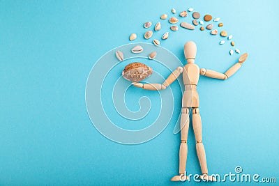 Wooden mannequin juggling sea shells on blue pastel background. copy space Stock Photo